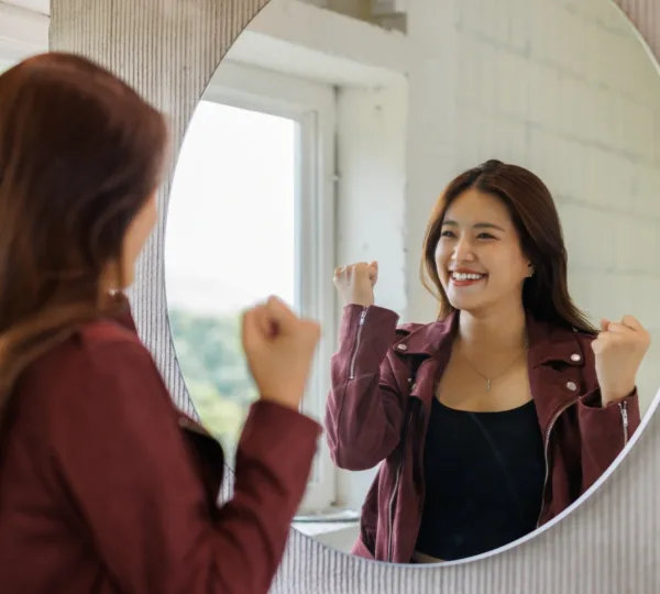 Mujer sonriendo con los puños en alto frente al espejo, ganando confianza en sí misma